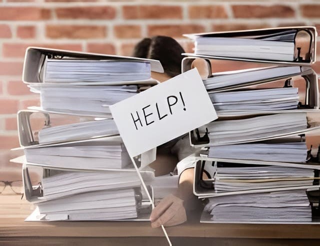 Iemand steekt een vlaggetje met het woord HELP omhoog tussen hoge stapels ordners.
